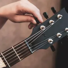 Hand tuning a black electric guitar headstock with tuning pegs and strings.