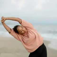 Femme en posture qi gong, s'étirant sur la plage au lever du soleil.