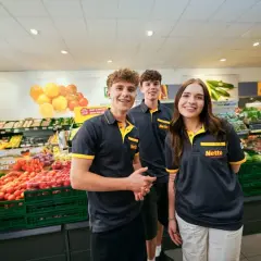 Drei junge Mitarbeiter lächeln in einem Supermarkt. Sie tragen Arbeitskleidung mit dem Netto-Logo. Die Ausbildung zum Elektroniker bietet ein gutes Gehalt netto.