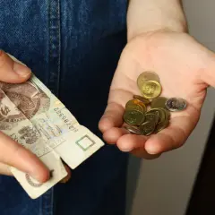 Dłoń trzyma banknot z widocznym klejeniem i garść monet. Czy sklejony banknot przyjmą w sklepie?