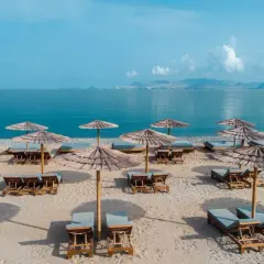 Plaża w Kefalos, Grecja. Leżaki i parasole z trawy morskiej czekają na gości, a turkusowe morze lśni w słońcu.
