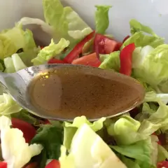 Löffel mit Balsamico Dressing über frischem Salat mit Tomaten und Paprika.