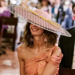 Peinado ondas invitada boda: mujer con sombrero de ala ancha y vestido naranja, sonriendo.