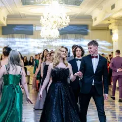Elegancki strój do poloneza: para młodych ludzi w balowych kreacjach, otoczona przez innych uczestników balu.