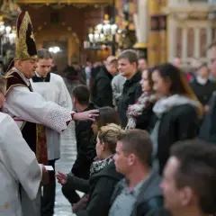 Biskup udziela sakramentu bierzmowania. Czy świadek do bierzmowania musi być pełnoletni? Wierni czekają w kościele.