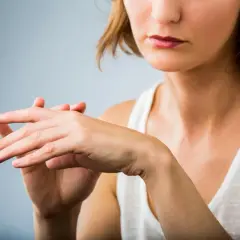 Kobieta dotyka swojej dłoni, jakby odczuwała dziwny ból skóry przy dotyku.