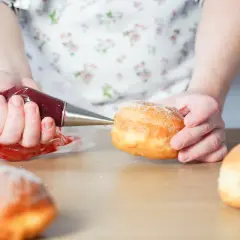 Hände füllen mit Marmelade gefüllte, zuckerbestäubte **bolas de fraile** mit einem Spritzbeutel.