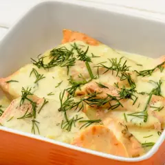 Pyszna ryba zapiekana serem i koperkiem w pomarańczowej miseczce.