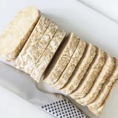 Pokrojony w plastry tempeh, czyli fermentowana soja, leży obok noża. To świetny składnik do wegańskich dań.