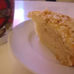 En bit gammaldags kardemummakaka med nötter på en vit tallrik, bredvid en mugg med texten "MAMMA".
