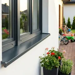 Eleganckie parapety zewnętrzne aluminiowe podkreślają nowoczesny wygląd domu. W tle plac zabaw i rowery.