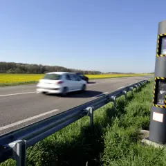 Un radar de vitesse sur le bord d'une route de campagne, avec des champs de colza jaunes et des voitures en mouvement. Ces photos des différents radars rappellent la vigilance.