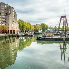 Widok na kanał z łodziami i nowoczesną architekturą, gdzie leży Rotterdam. W oddali czerwony most.