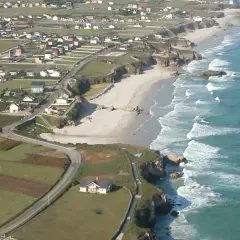 Vista aérea de la playa Longara en Lugo, con casas blancas y campos verdes bordeando la costa.