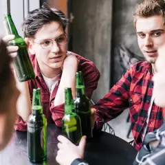 Młodzi ludzie przy stole, butelki piwa, początek alkoholizmu wśród młodzieży.