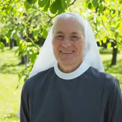 Lächelnde Nonne im Garten. Sie hat graue Haare und trägt eine graue Ordenskleidung mit weißem Schleier. Das Leben ist nicht fair, aber sie strahlt Hoffnung aus.