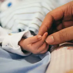 Dłoń dorosłego obejmuje maleńką dłoń dziecka. To obraz miłości i wsparcia, symbol nadziei dla rodzin z zespołem Patau.