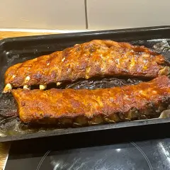 Två ugnsbakade kamben, glaserade och gyllene, ligger på en plåt. Doften av BBQ sprider sig i köket.
