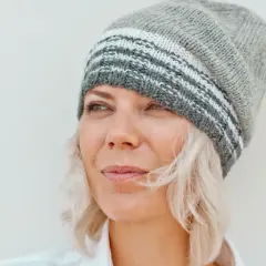 Frau mit blonden Haaren und Strickmütze, die nachdenklich in die Ferne blickt. Sie genießt ihr Leben mit 55 in Rente.