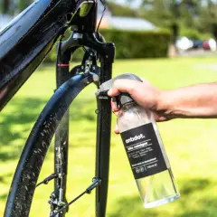 Hand sprüht Fahrradrahmen mit Reiniger ein. Sorgfältige Fahrrad Pflege für glänzende Ergebnisse im Freien.