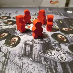 Czerwone pionki graczy walczą z zombie na planszy gry. W tle widać zniszczone budynki i barykady. To gra planszowa o tematyce atak zombie.