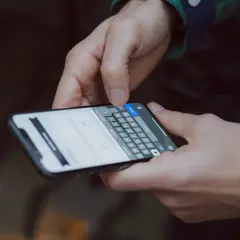 Dłonie trzymające smartfon z klawiaturą ekranową, jedna ręka naciska przycisk "Done".