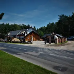 Budynek "Borowa Ciotka" w lesie, w trakcie remontu dachu. Obok droga, samochody i parking.