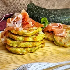 Deliciosas tortillitas de calabacín apiladas, coronadas con jamón serrano. Un plato fresco y sabroso.
