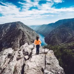 Niña en el mirador Vilouxe, contemplando un cañón con un río azul y montañas verdes bajo un cielo nublado.