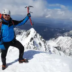 Szczęśliwy alpinista z czekanem na szczycie Rysów zimą. W tle rozległa panorama ośnieżonych gór.