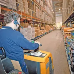 Mitarbeiter mit Headset führt Kommissionierauftrag per Sprachsteuerung (pick by voice) im Lager durch.