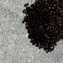 Ciemna plama oleju na asfalcie, świadcząca o wycieku oleju z uszczelniacza wału korbowego.