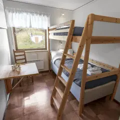 Enkel och mysig rum på vandrarhem Åre med våningssäng, litet bord och fönster med utsikt över grönskande landskap.