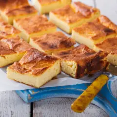 Pyszny skyrnik pieczony z budyniem, pokrojony w kostkę, prezentuje się apetycznie na niebieskiej desce.