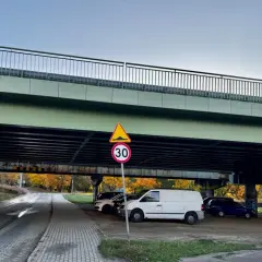 Pod estakadą zaparkowane są samochody. Widoczny znak ograniczenia wysokości 2,8m i znak ograniczenia prędkości do 30 km/h.