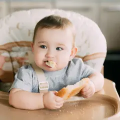 Słodki maluch w krzesełku z chlebkiem w rączce. Zastanawiasz się, jaki chleb dla rocznego dziecka będzie najlepszy? Ten wygląda apetycznie!