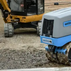 Niebieski walec do gruntu Weber MC 85 pracuje na budowie obok żółtej koparki.