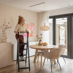 Mujer en escalera ajustando una lámpara colgante de dos luces sobre una mesa de comedor.