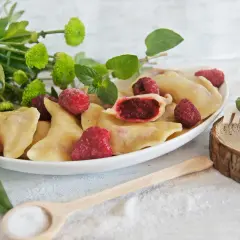 Pyszne pierogi z malinami, ozdobione świeżymi malinami i zielonymi listkami. Idealne na letni deser.