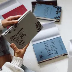 Une personne tient une jaquette de livre "Hit delete". D'autres livres sont disposés autour.