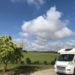 Camping-car en France, sous un ciel bleu et nuageux, avec un champ de tournesols en arrière-plan. La passion du voyage en camping-car.
