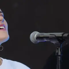 Taya Smith singt mit geschlossenen Augen und In-Ear-Monitoring. Ein Mann mit Kappe steht im Hintergrund.