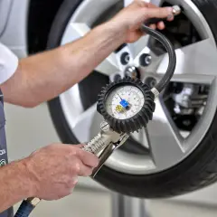 Mechanik sprawdza ciśnienie w oponie, używając manometru. To ważne, by wiedzieć, gdzie są czujniki ciśnienia w oponach i jak je kontrolować.