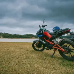 Czerwono-czarny motocykl z niebieskim kaskiem na siedzeniu, gotowy do jazdy nad jeziorem.