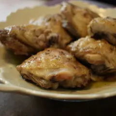 Plusieurs hauts de cuisse de poulet rôtis, assaisonnés d'herbes, reposent sur une assiette en céramique crème.