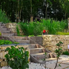 Moderne Gartenaufteilung Ideen mit Gabionenmauern, Steintreppen und üppiger Bepflanzung. Ein Kamin aus Steinen integriert sich harmonisch.
