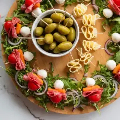 Kolorowe przekąski sałatki na imprezę: szaszłyki z pomidorkami, mozzarellą, salami i marchewką, oliwki i serowe zawijasy.