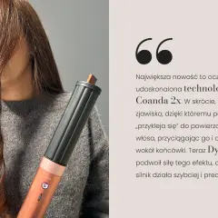 Kobieta z kręconymi włosami trzyma urządzenie Dyson Airwrap z technologią Coanda 2x, która ułatwia stylizację.