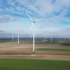 Wiatraki na tle błękitnego nieba z chmurami, na tle pól uprawnych.