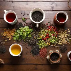 Tasses de thé noir fumant, entourées d'herbes fraîches, de baies rouges et de feuilles séchées. Une invitation à savourer une infusion réconfortante.